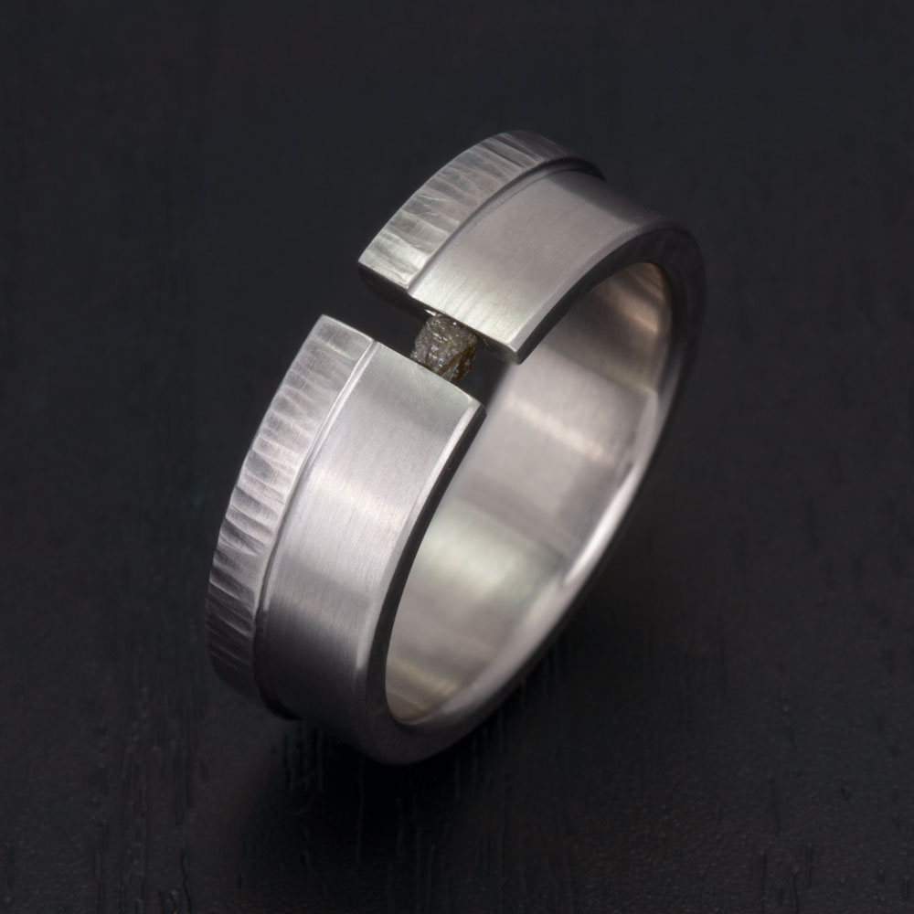 Highlighting the ring's durability and authenticity with its stainless steel composition and genuine rough diamond cube centerpiece.