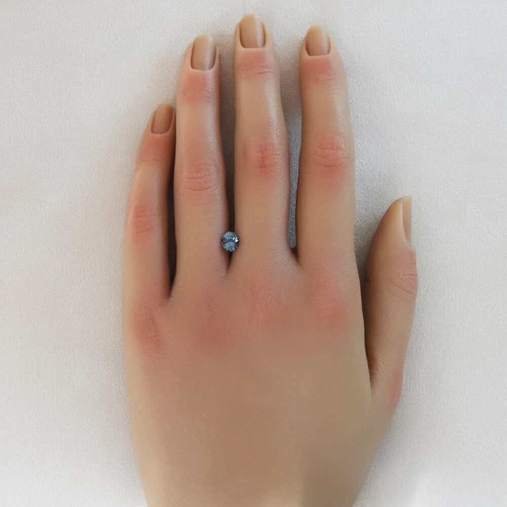 An image of a color changing blue and green sapphire displayed on a woman's hand.